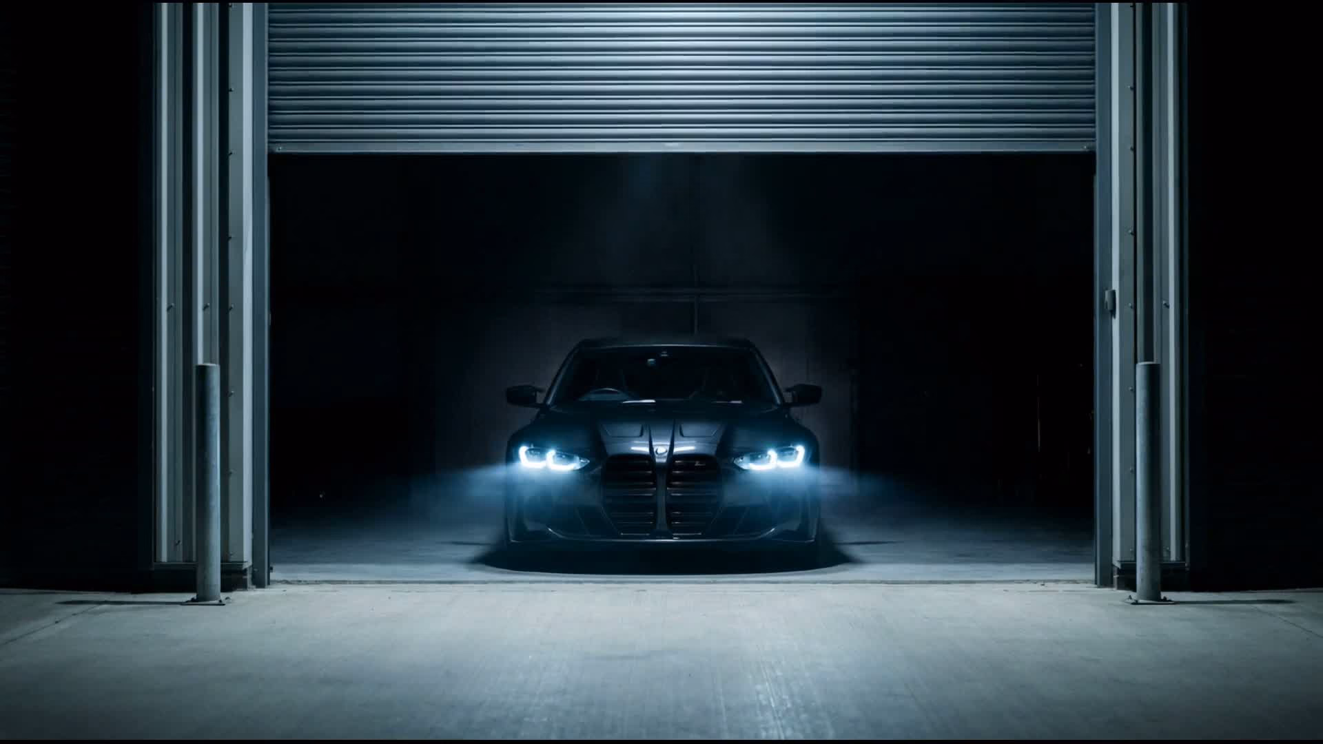 A BMW M3 lit by its own headlights in the darkened O&R Autohaus unit, roller shutter half-raised